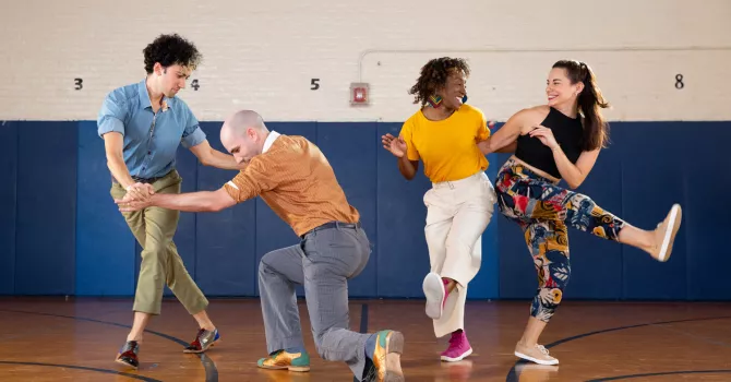 Four swing dancers in colorful costumes dancing in a gym