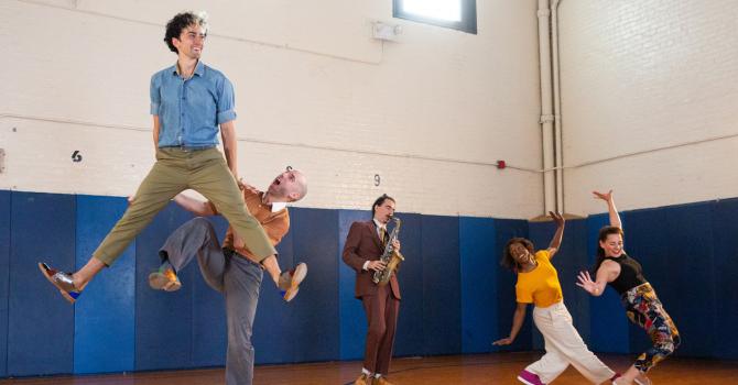 Four swing dancers in a gym with a saxophonist