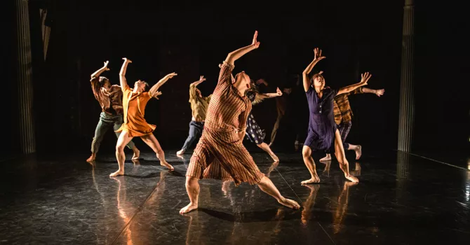 Eight modern dancers on a black stage in a group position