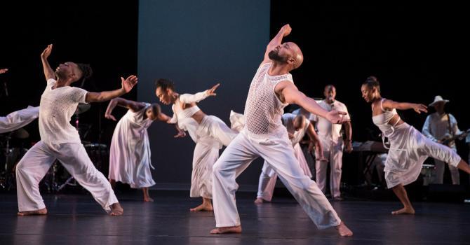 A group of dancers wearing all white perform on stage.