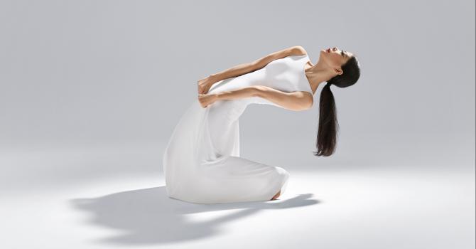 A single modern dancer posing in a white dress and a black ponytail