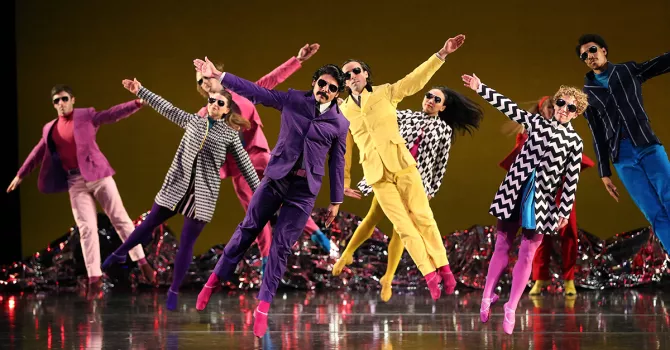 Dancers in colorful costumes tilting to the side with arms out