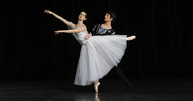 Ballet dancer in white dress on pointe with a dancer holding her waist
