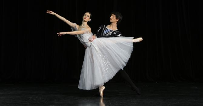Ballet dancer in white dress on pointe with a dancer holding her waist