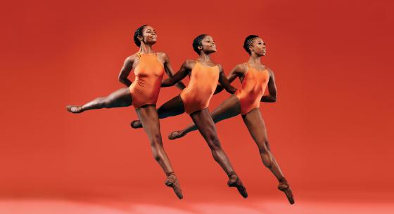 Three female dancers perform together in front of an orange background.
