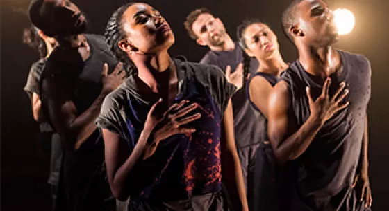 Five dancers in black dress under a spotlight