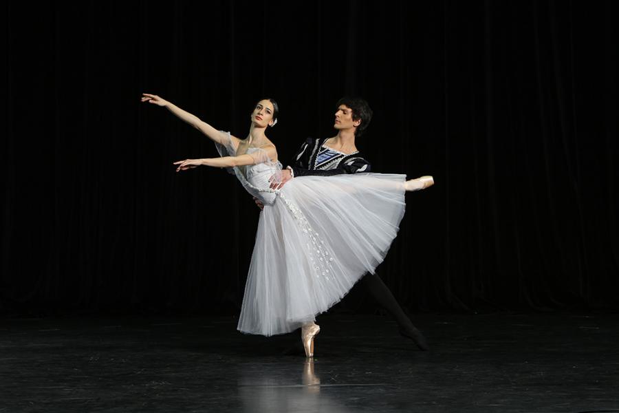 Ballerina on pointe in arabesque, arms out with her partner holding her waist