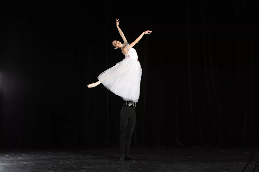 Lead dancer poses while lifted high above the stage, her partner is obscured by her gown and it looks as if she's floating above the stage