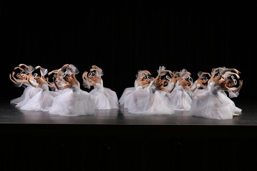 Front view of the corps de ballet in bright white, on one knee leaning to the side with arms circling their heads
