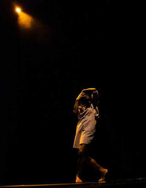 A dancer performs on stage with one dim spot light shining down on them.