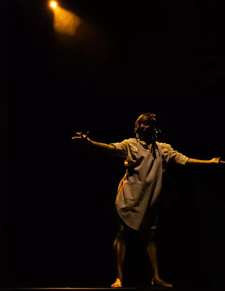 A dancer performs on stage with one dim spot light shining down on them.