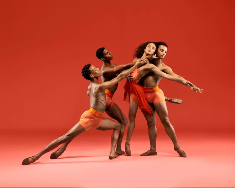 Four Dance Theatre of Harlem dancers perform together in front of an orange background.