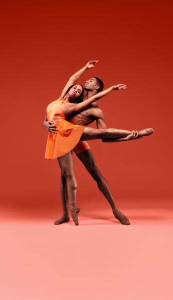 Two dancers perform together in front of an orange background.
