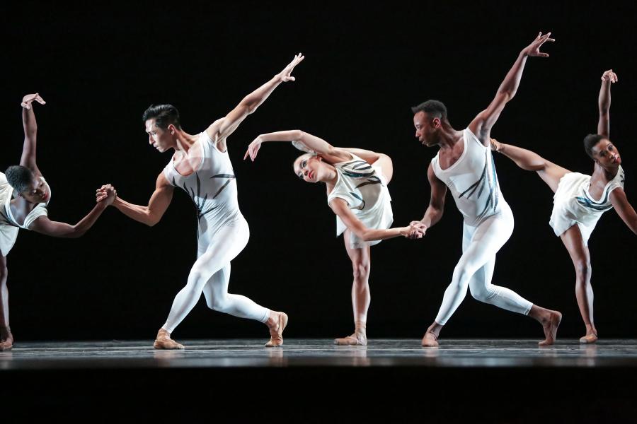 Dance Theatre of Harlem dancers wearing white perform on stage with a black background.