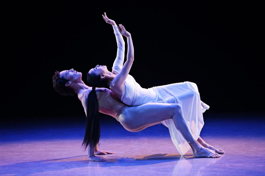 Two dancers perform on a purple lit stage