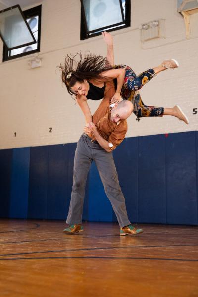 Two dancers perform together in a gymnasium setting.