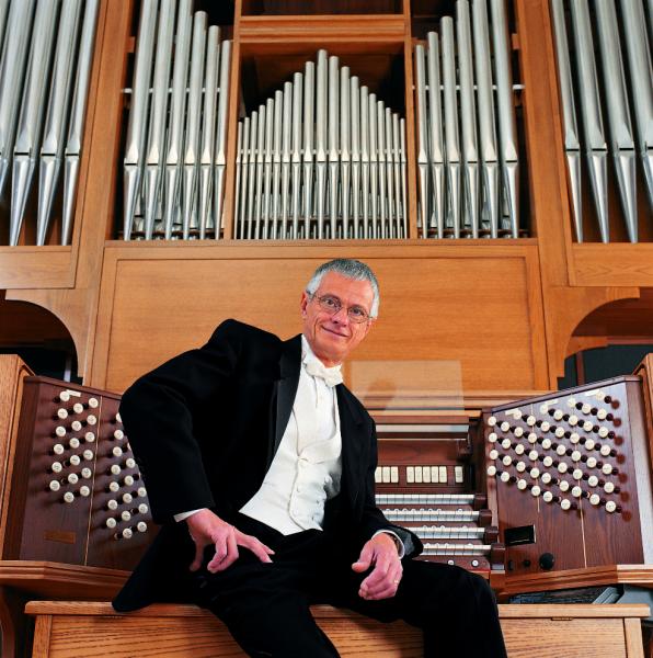 Olivera sitting in front of the organ with a hand on his hip, leaning against the keys