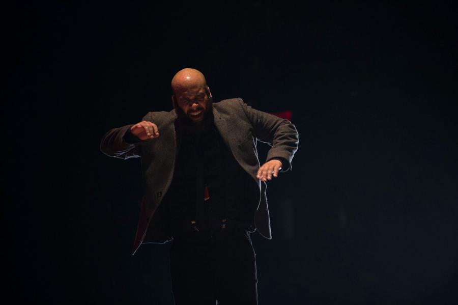 A tap dancer performs against a dark background.