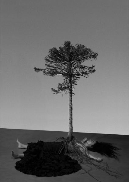 A black and white image depicts a person laying on the floor with their arms overhead. A tree's roots cover the person's body and the tree appears to be coming out of the person's torso. 