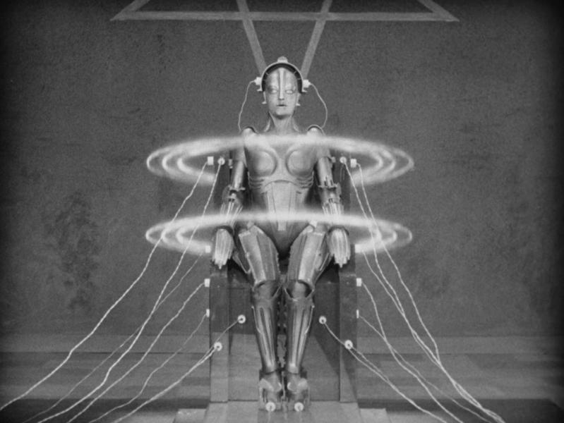 A human-like figure sits in a chair with wires connected to it. Two large circles float around the shoulders and waist of the figure.