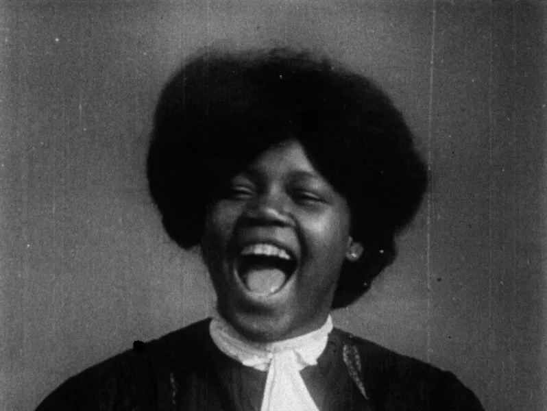 A close image of a person laughing with their mouth open. They have short black hair and are wearing black and white.