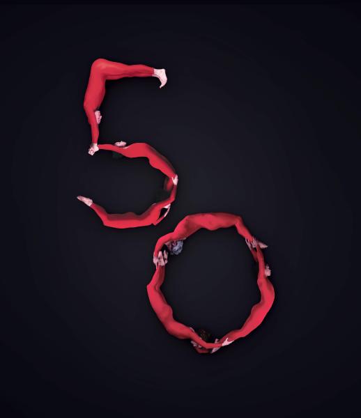 Six dancers wearing red make the shape of a number 50 on the ground of a black stage.