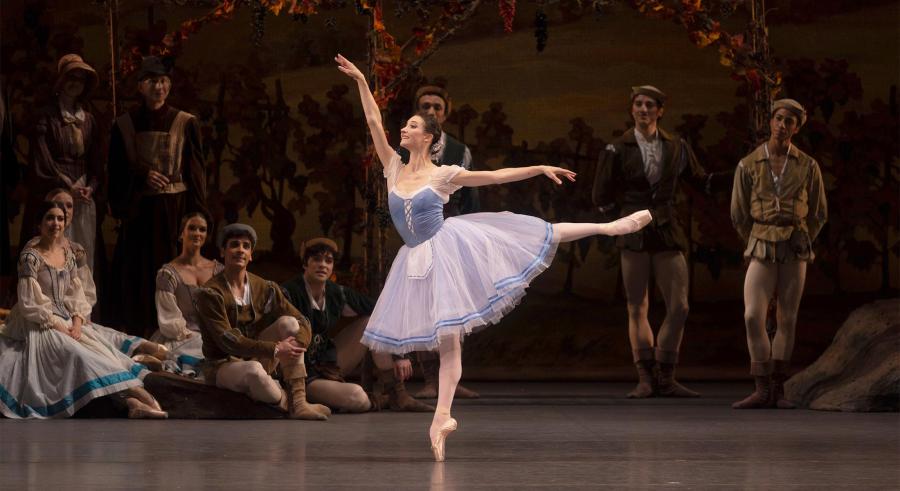 A ballerina dances as other performers watch from the edge of the stage