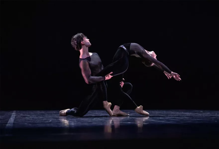 Couple in black bodysuits. One dance on his knee supporting the other in a deep backwards arch.