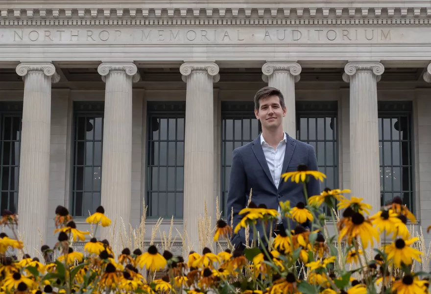 Greg stands in front of the columns of Northrop outside by the flowers.
