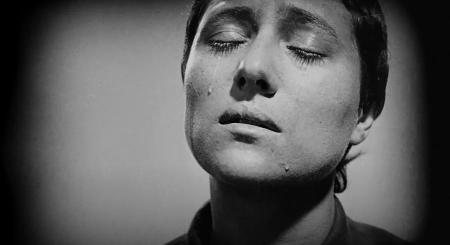 Black and white film still of a closeup of Joan of Arc with her eye closed and tears streaming down her face.