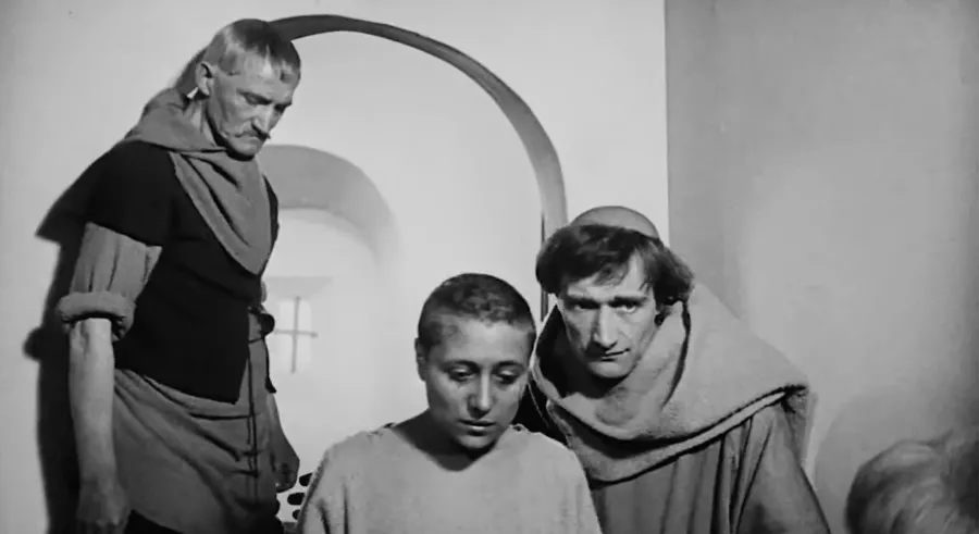 Black and white film still of 2 clergy-looking men around the Joan of Arc charecter, giving comfort.
