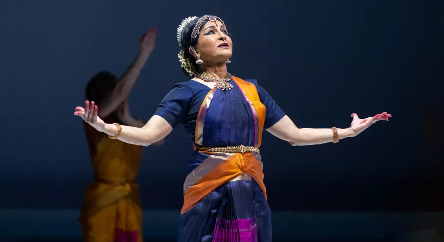 Dancer with both arms outstretched under a spotlight.