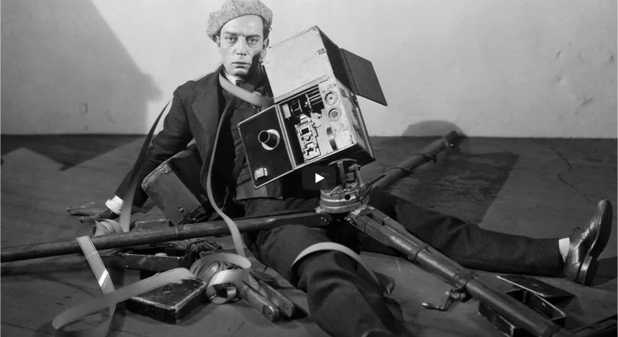 Black and white film still of Buster Keaton as The Cameraman sitting on the floor with opened camera spilling film all around him.