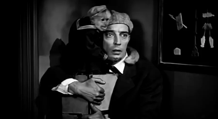 Buster Keaton emotes at something unseen, a monkey in a sailor suit wrapped around his shoulders. From a still from The Cameraman.