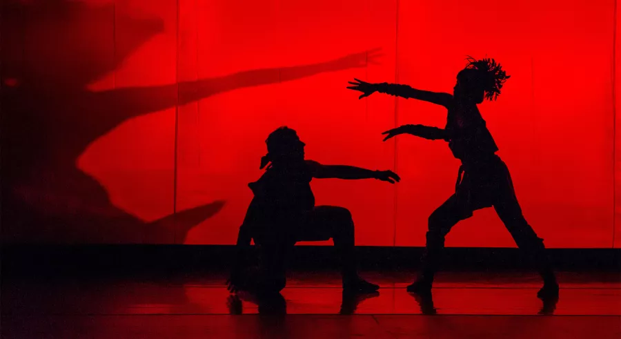Silhouettes of dancers strike dramatic poses against a glowing red backdrop.