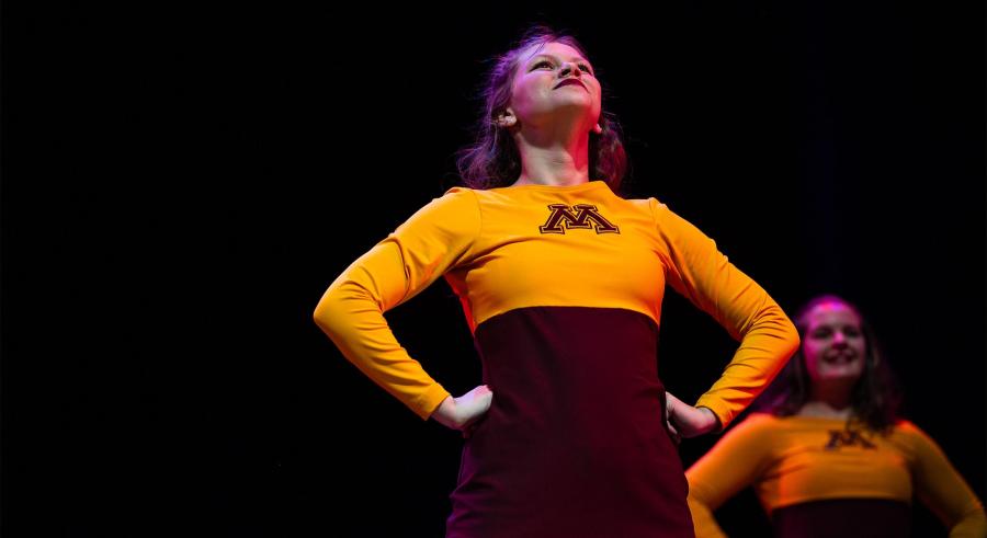 Performer stands with hands on her hips, a University M on her yellow shirt.