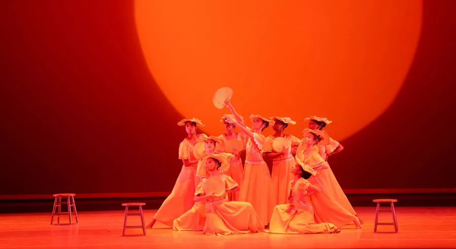 Group of dancers onstage in a cluster in bright orange lighting.
