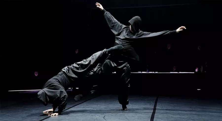 Two company members dancing. Left: head down, body lifted, legs extended. Right: arms up. 