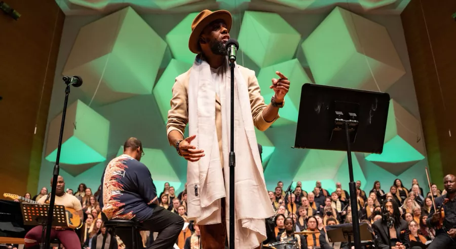 Joe Davis wearing a white stole and singing in front of the VocalEssence WITNESS choir at Orchestra Hall.