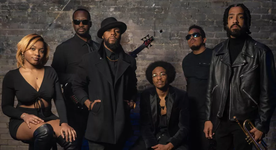 Members of The Poetic Diaspora in all black posing in front of a gray background. 