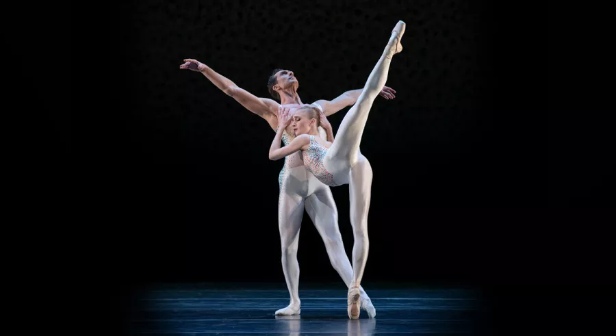 Dancer with one leg kicked high, embracing another dancer who is leaning backward. 