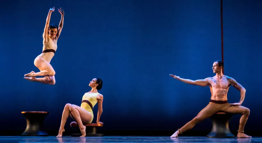 One dancer mid-leap with two other dancers to the right watching.