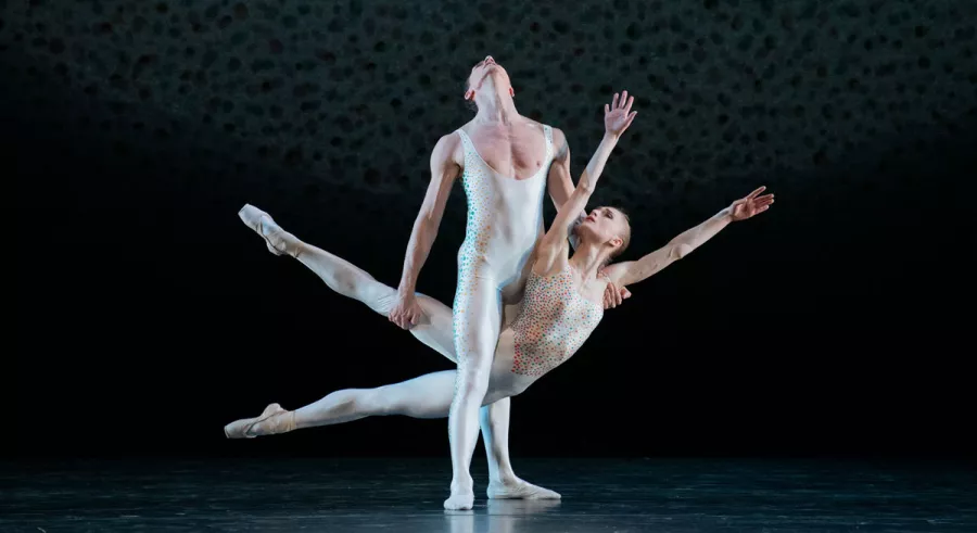One dancer stands supporting another dancer between their legs with the lower dancer's arms and legs oustretched.