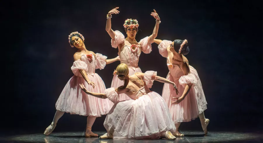 Four dancers posing in a circle in front of a black background onstage. 