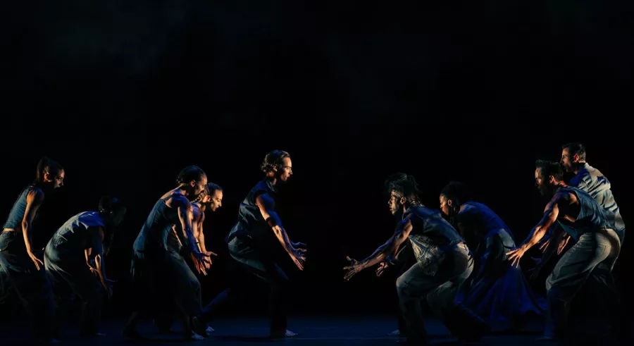 Dimly lit dancers all facing toward the center of the stage. 