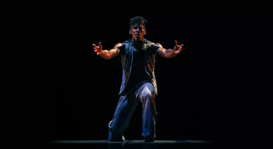 Dancer in front of a black background with their arms outstretched in front of them. 