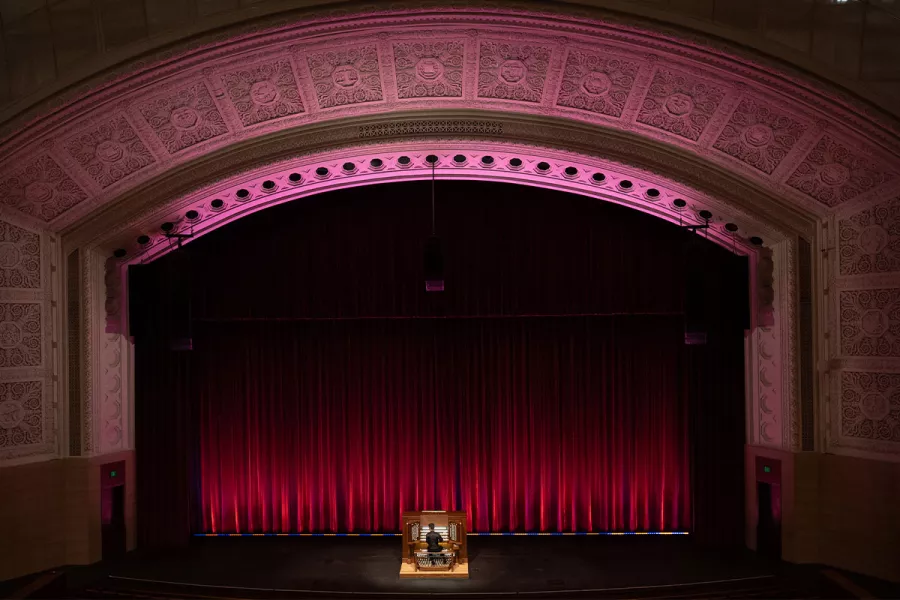 An man playing a pipe organ on the Northrop stage in front of a red curtain.