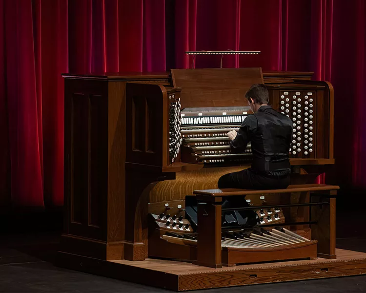 Greg playing the organ on the Northrop stage with the red curtain in the background.