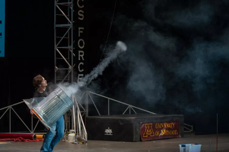 A man holds a metal trash can as a ring of smoke shoots out of one end.