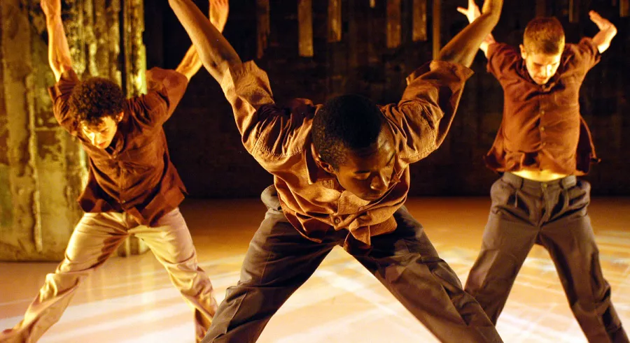 Three dancers leaning forward, legs streched, arms behind their backs. 
